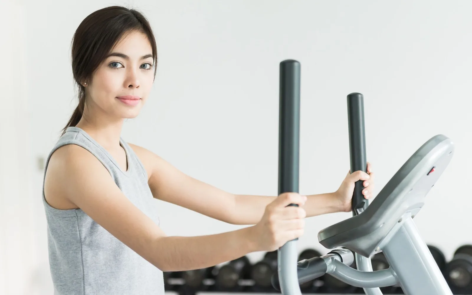 Persona pedaleando en una bicicleta estática en un gimnasio, con la zona de pesas al fondo