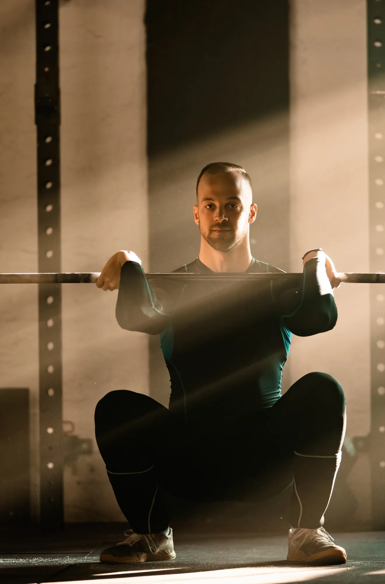 Hombre haciendo una sentadilla con la barra junto a la ventana del gimnasio